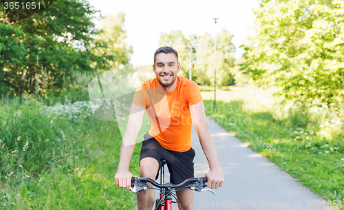 Image of happy young man riding bicycle outdoors