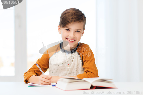 Image of smiling student boy writing to notebook at home