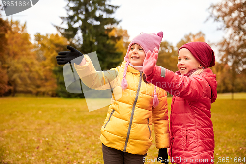 Image of two happy little girls waving hand in autumn park