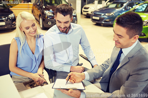 Image of happy couple with car dealer in auto show or salon