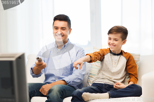 Image of smiling father and son watching tv at home