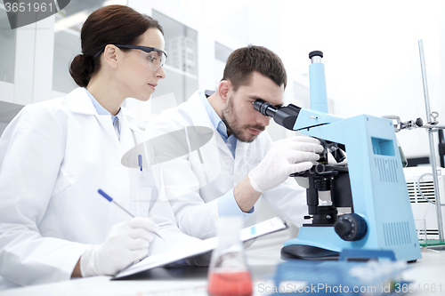 Image of scientists with clipboard and microscope in lab