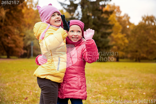 Image of happy little girls waving hands in autumn park