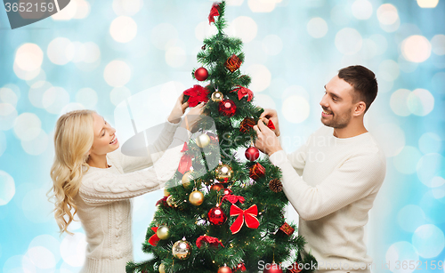 Image of happy couple decorating christmas tree over lights