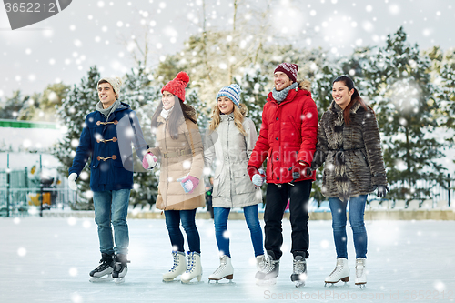 Image of happy friends ice skating on rink outdoors