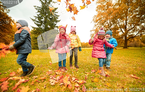 Image of happy children playing with autumn leaves in park