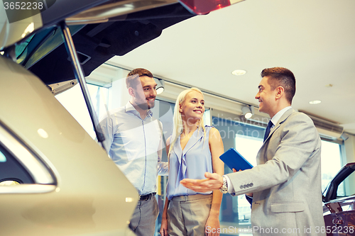 Image of happy couple with car dealer in auto show or salon