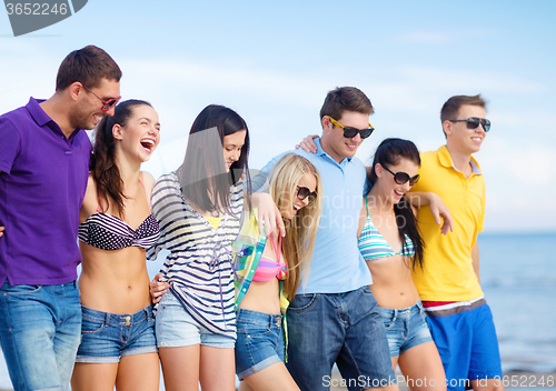 Image of group of happy friends walking along beach