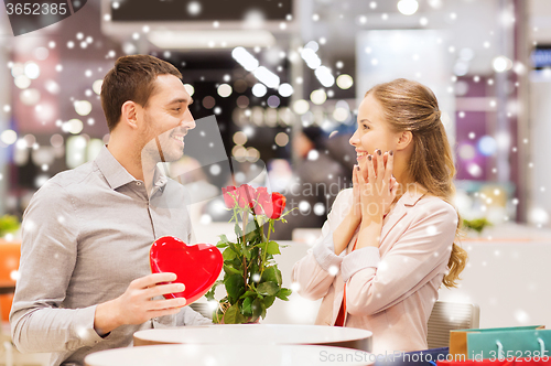 Image of happy couple with present and flowers in mall