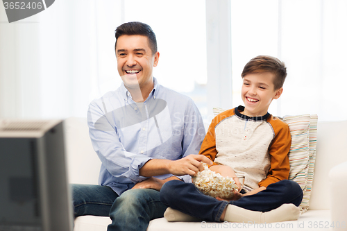 Image of smiling father and son watching tv at home