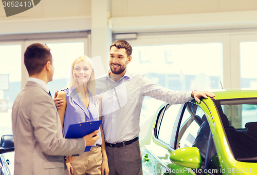 Image of happy couple with car dealer in auto show or salon