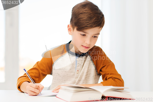 Image of student boy with book writing to notebook at home