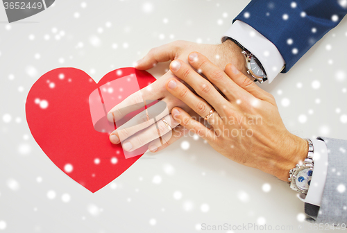 Image of close up of male gay couple hands with red heart