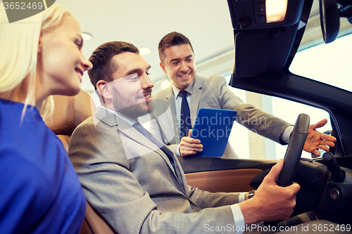 Image of happy couple with car dealer in auto show or salon