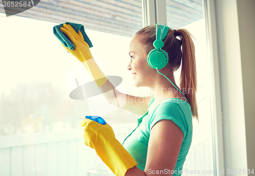 Image of happy woman with headphones cleaning window