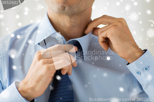 Image of close up of man in shirt adjusting tie on neck