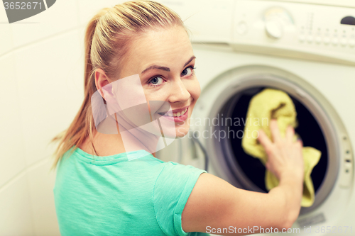 Image of happy woman putting laundry into washer at home