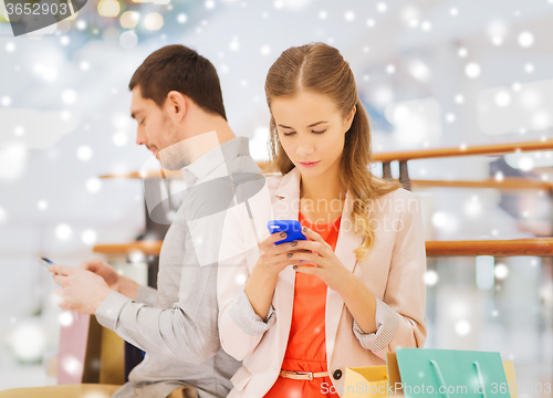 Image of couple with smartphones and shopping bags in mall