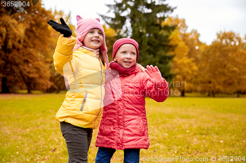 Image of two happy little girls waving hand in autumn park