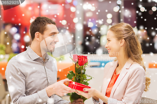 Image of happy couple with present and flowers in mall