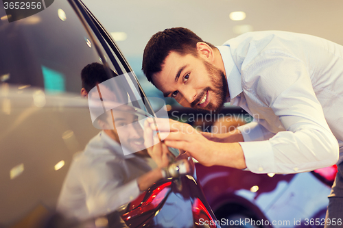 Image of happy man touching car in auto show or salon