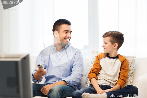 Image of smiling father and son watching tv at home