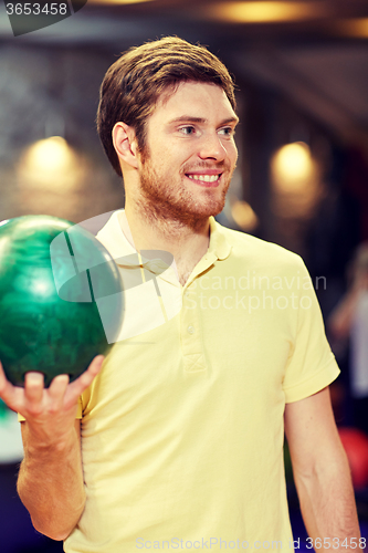 Image of happy young man holding ball in bowling club