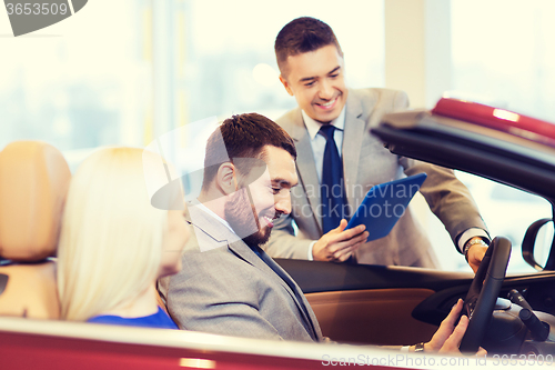 Image of happy couple with car dealer in auto show or salon