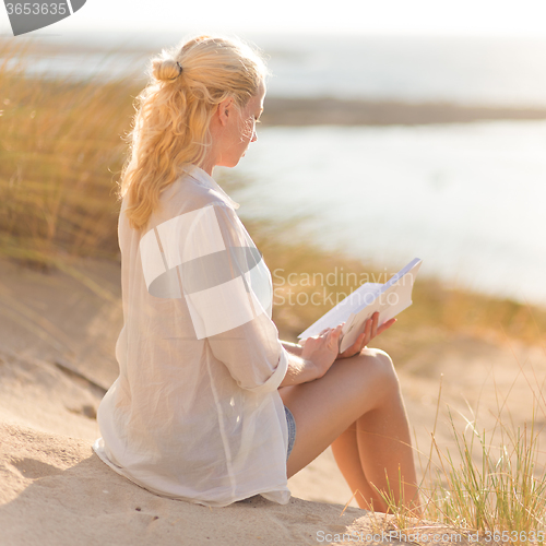 Image of Woman enjoys reading on beautiful sandy beach.