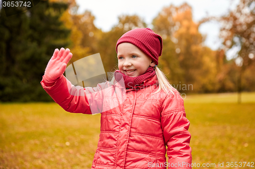 Image of happy little girl waving hand in autumn park