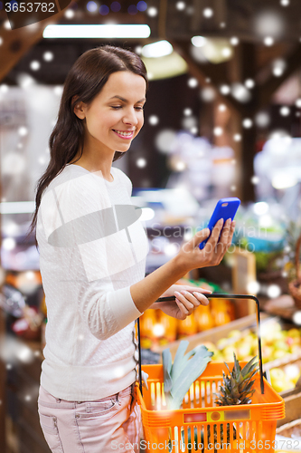 Image of happy woman with basket and smartphone in market