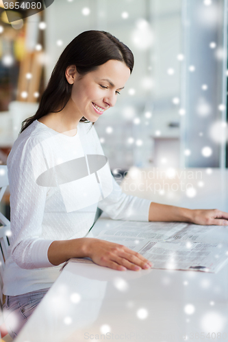 Image of smiling young woman reading newspaper at cafe