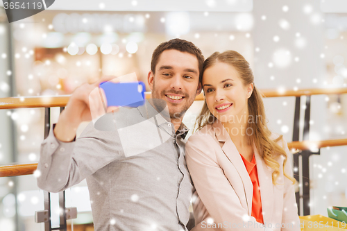 Image of happy couple with smartphone taking selfie in mall