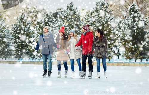 Image of happy friends ice skating on rink outdoors