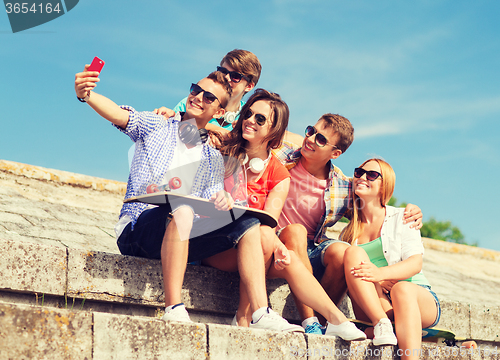 Image of group of smiling friends with smartphone outdoors