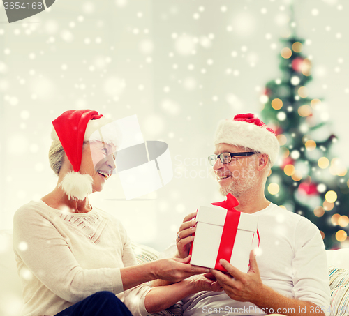 Image of happy senior couple in santa hats with gift box