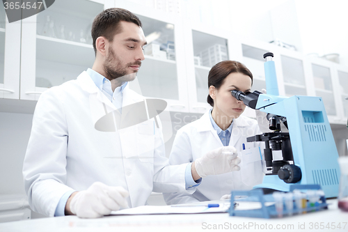 Image of scientists with clipboard and microscope in lab