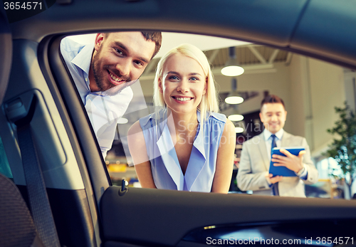 Image of happy couple with car dealer in auto show or salon