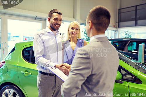 Image of happy couple with car dealer in auto show or salon