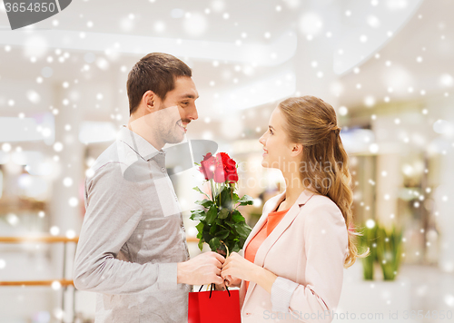 Image of man giving woman red roses and present in mall