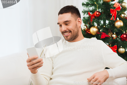 Image of smiling man with smartphone at home for christmas