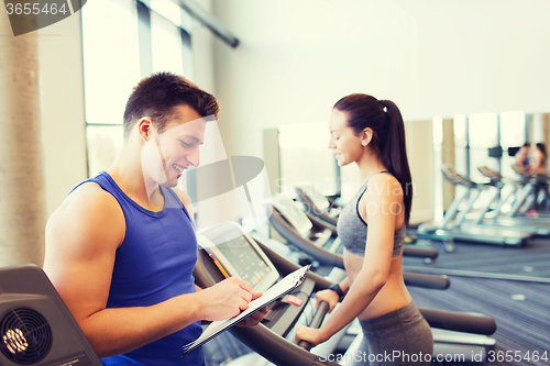 Image of happy woman with trainer on treadmill in gym