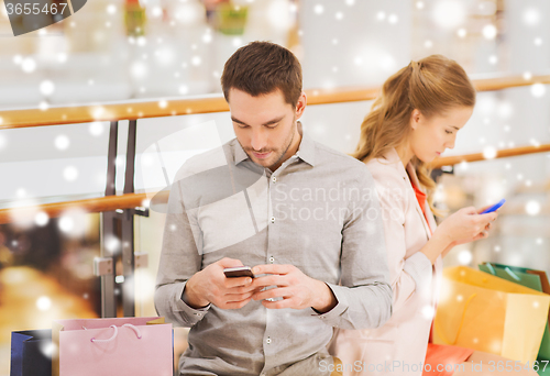 Image of couple with smartphones and shopping bags in mall