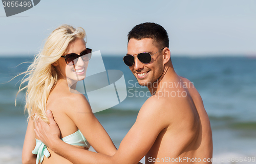 Image of happy couple in swimwear sitting on summer beach