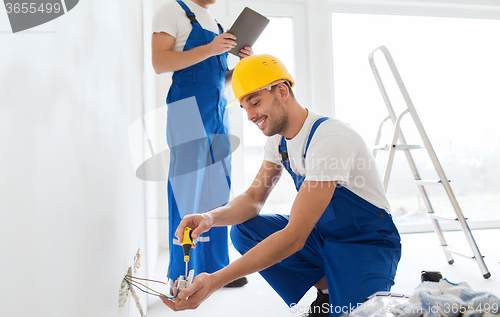 Image of builders with tablet pc and fixing wiring indoors