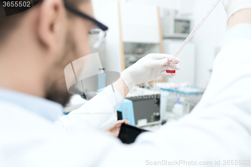 Image of close up of scientist with tube and pipette in lab