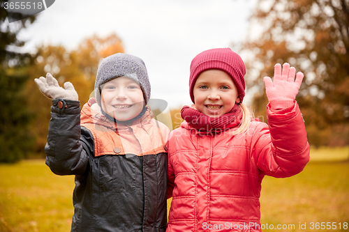 Image of happy girl and boy waving hands in autumn park