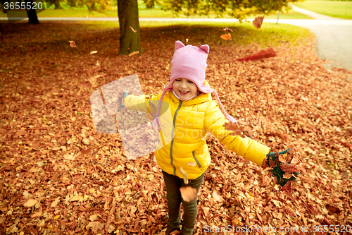 Image of happy girl playing with autumn leaves in park