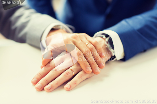 Image of close up of gay couple hands with wedding rings on