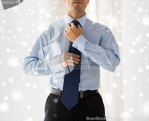 Image of close up of man in shirt adjusting tie on neck